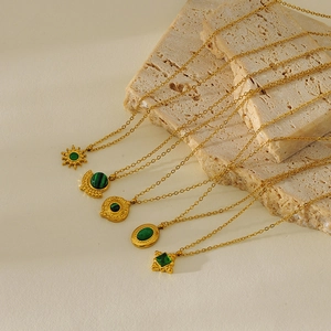Detail of five vintage gold-plated necklaces with emerald and malachite pendants on stone