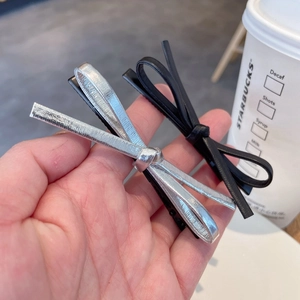 Detail shot of a silver glossy and black faux leather bow hair clip set held by hand