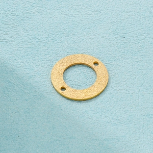 Detail of matte gold circular pendant with double holes on a light blue background