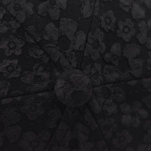 Dettaglio macro del tessuto jacquard nero con ricami floreali e bottone superiore