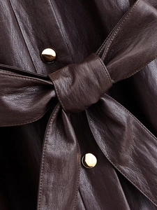 Detail of dark brown faux leather coat featuring gold buttons and tied waist belt texture