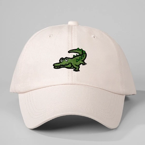 Close-up of green cartoon crocodile embroidery on a light pink cotton baseball cap