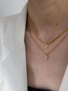 Detail of layered gold initial R necklaces with zircon micro-paving on a model
