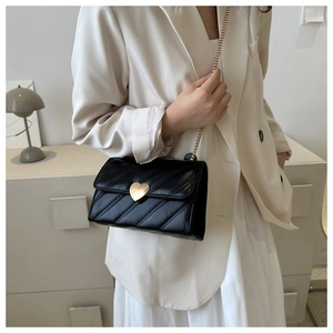 Elegant black quilted crossbody bag with heart lock on a stylish white suit outfit