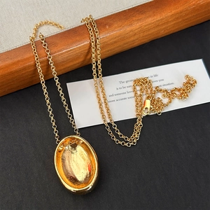 Minimalist gold oval pendant necklace with cross chain on a professional black background