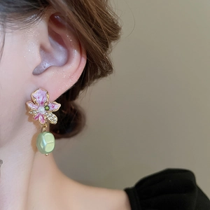 Detailed close-up of pink flower earrings with green pearl drop on model's ear