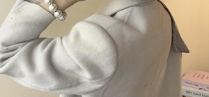 Detail shot of beige wool coat fabric texture and large pearl bracelet hair tie accessory