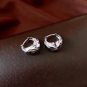 Glossy silver U-shaped hoop earrings with irregular pleated texture on leather background