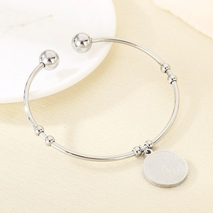 Detail of silver stainless steel open bangle with beads and circular engraved religious charm