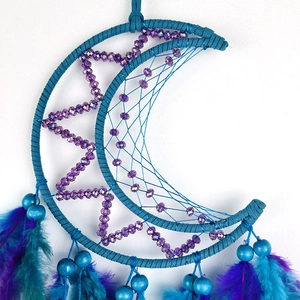 Blue and purple moon dreamcatcher with star weaving and hanging feathers on white wall