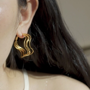 Minimalist irregular geometric wavy gold hoop earrings worn by a model in a lifestyle shot