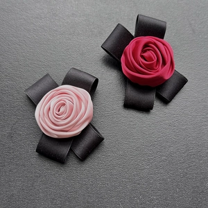 Pink and dark red satin rose brooches with black ribbon bows on a textured background