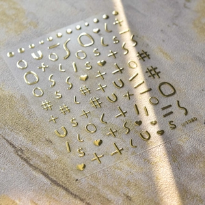 Macro de pegatinas doradas para manicura con letras y corazones sobre piedra clara