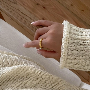 Detail showing a minimalist gold beaded ring worn on finger with soft knit background