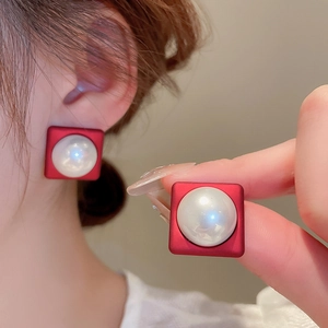 Detail of red matte square earrings featuring a lustrous central pearl on model's ear