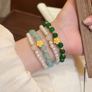 Detalle de pulseras de piedras naturales y perlas con colgantes de flores doradas.