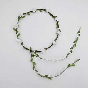 Detailed close-up of white fabric flowers and green leaves on a bridal flower crown headband