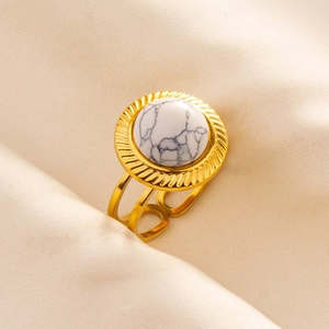 Detail eines verstellbaren Goldrings mit weißer Marmorstein-Einlage auf beigem Stoff