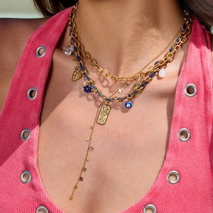 Détail de colliers dorés superposés avec cordon bleu, pendentif soleil et breloques cœur