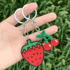 Detail of handmade beaded strawberry and cherry keychains on a natural grass background