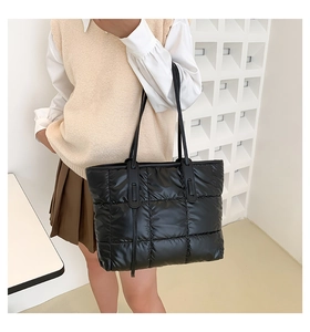 Detailed view of black quilted puffer tote bag worn over the shoulder by a model