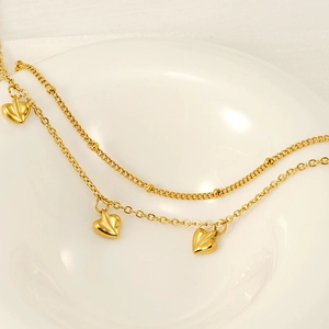 Detail of 18K gold double-layer anklet featuring heart charms and bead chain texture
