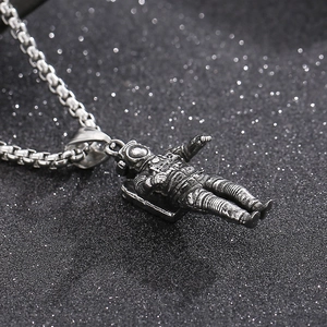 Macro view of silver astronaut pendant with box chain on textured black background