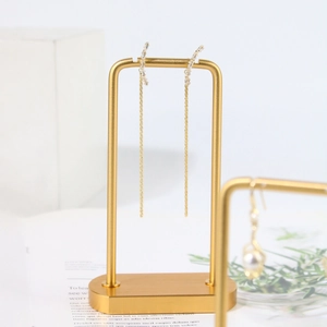 Close-up of golden tassel earrings with white zircons on a matte gold metal display stand