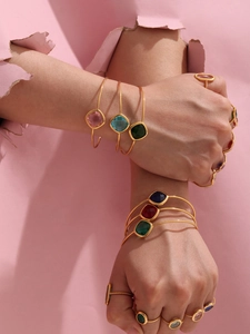 Close-up of model wearing gold open bangle and multi-color faceted glass gem rings