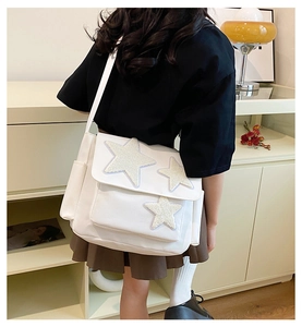 Back view of a white canvas messenger bag with fuzzy star patches worn by a model in a room