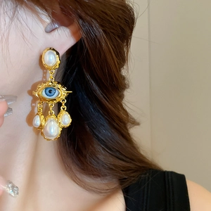 Detail of vintage gold eye earrings with blue iris and hanging teardrop pearls on model