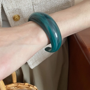 Close-up of a wide green acrylic open cuff bracelet with marbled texture on a female wrist