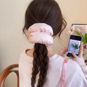 Close-up of pink oversized satin scrunchie on a braided ponytail in home setting