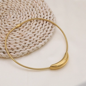 Macro detail of a minimalist gold curved tube pendant on a glossy snake chain necklace