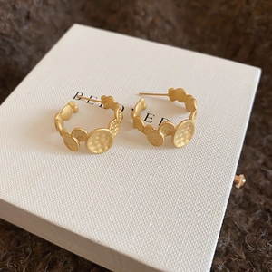 Detailed macro view of gold hammered C-shape earrings with irregular round metal discs