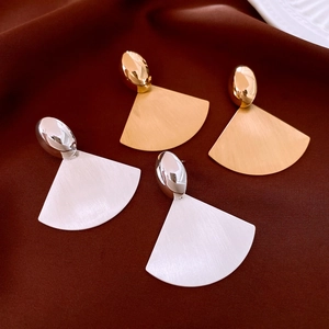 Close-up of brushed metal fan earrings in gold and silver on brown velvet background