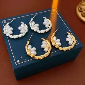 Detail view of gold and silver C-shaped hoop earrings with white pearls on a blue box