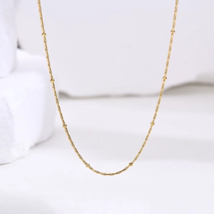 Vue macro d'un collier en acier inoxydable doré 1mm avec perles sur support blanc pur