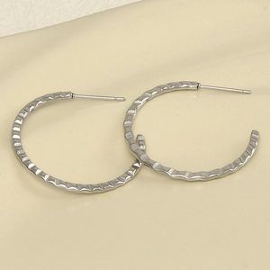 Macro detail of silver stainless steel hoop earrings with textured wavy metal surface