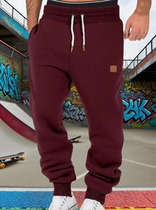 Detail of burgundy jogger pants featuring drawstring waist and ribbed cuffs on skateboard court
