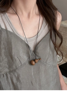 Détail d'un pendentif gourde en bois naturel sur un cordon noir porté sur du vert