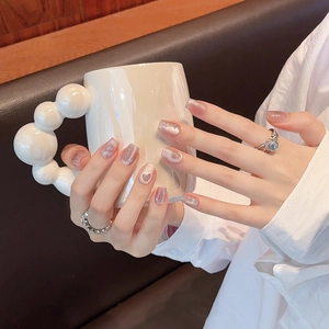 Pink heart cat-eye press-on nails with glitter French tip style on a model holding a cup