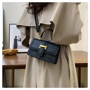 Detail of black woven leather handbag with gold buckle and stylish wide shoulder strap