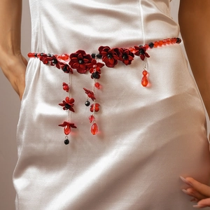 Close-up of red acrylic flower waist chain with crystals on white satin dress