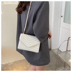 Detailed view of white V-quilted crossbody bag with elegant pearl strap on model
