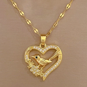 Macro shot of gold-plated heart necklace featuring a crystal-studded bird on a branch detail