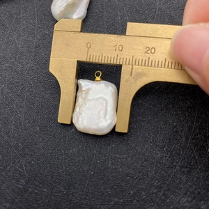 Macro shot of a 15mm white baroque pearl pendant measured with a brass caliper tool