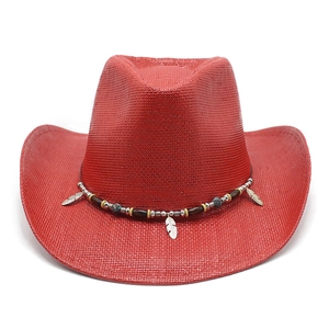 Detail of red cowboy straw hat featuring wide brim and decorative beaded band with feathers