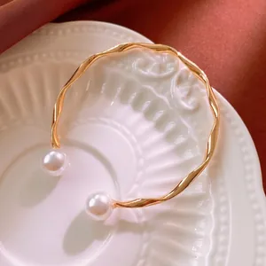 Elegant gold wave bangle with white faux pearls on a vintage ceramic display