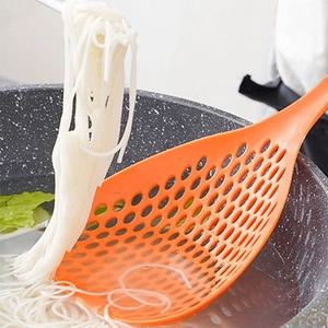 Orange large slotted spoon lifting noodles from a stone pot in a kitchen setting